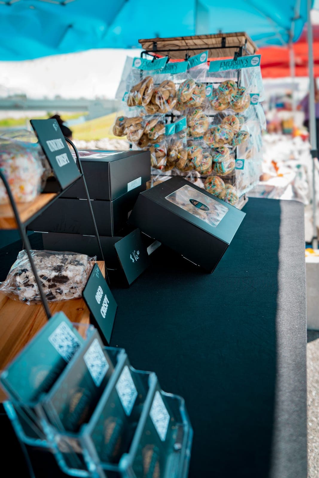 Black cookie gift boxes and a rack of bagged cookies on the market table