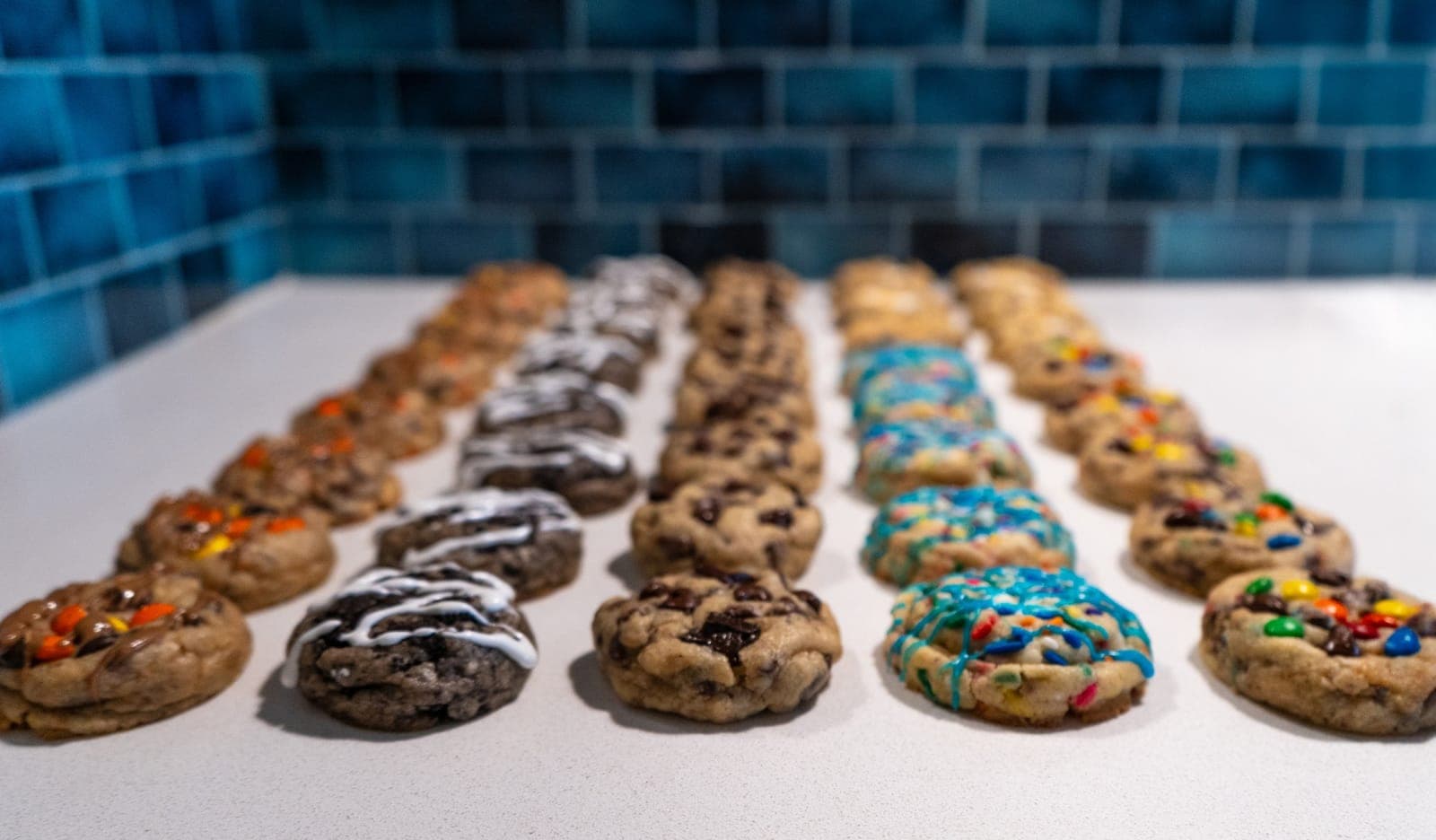 Rows of mini cookies in assorted flavors on a counter in front of teal tile