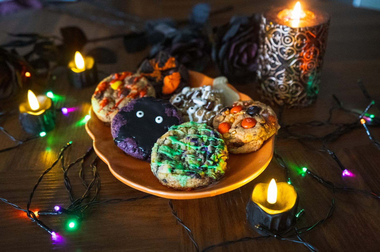 Halloween cookies piled on an orange pumpkin plate beside a lit candle