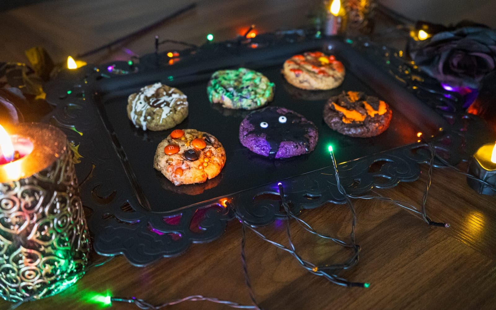 Six Halloween cookies on a black tray with candles and string lights