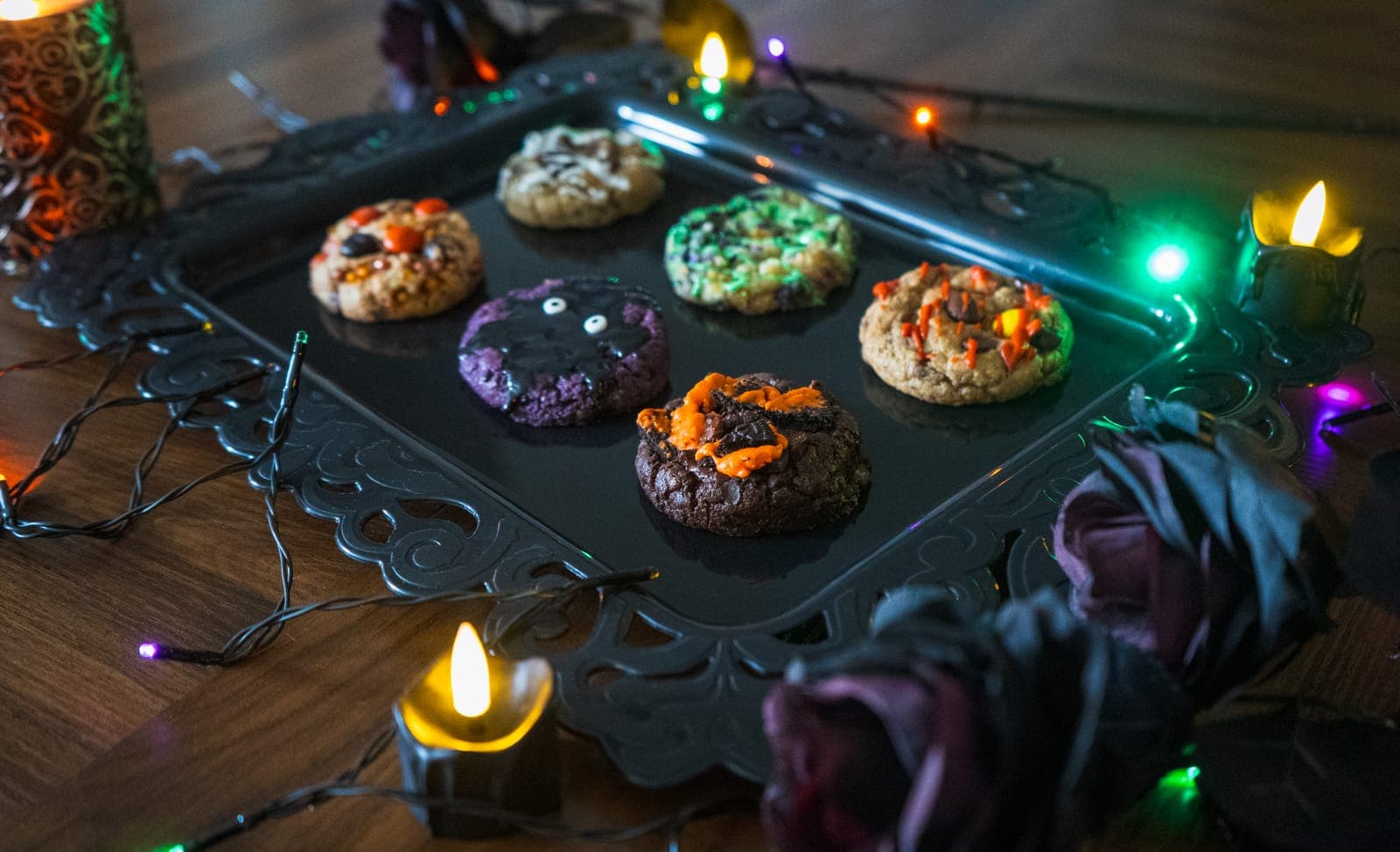 Halloween cookies on a black tray next to black roses and string lights