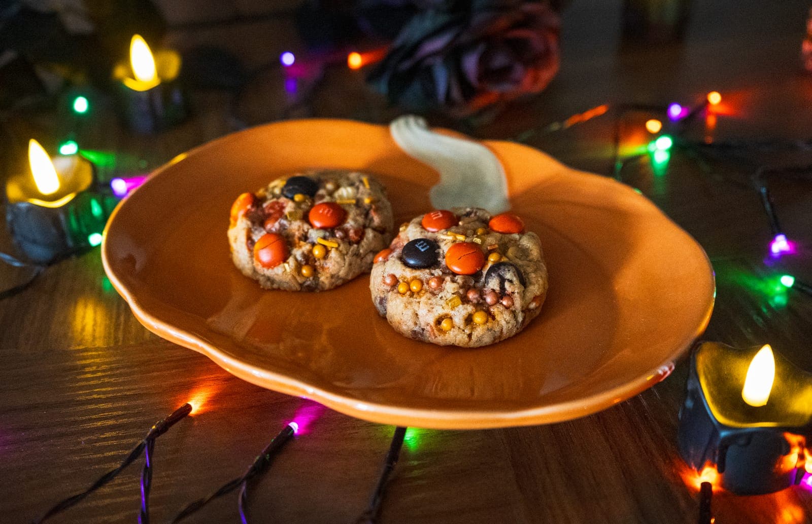 Two Fall M&M cookies with orange and brown M&Ms and fall sprinkles on a pumpkin plate