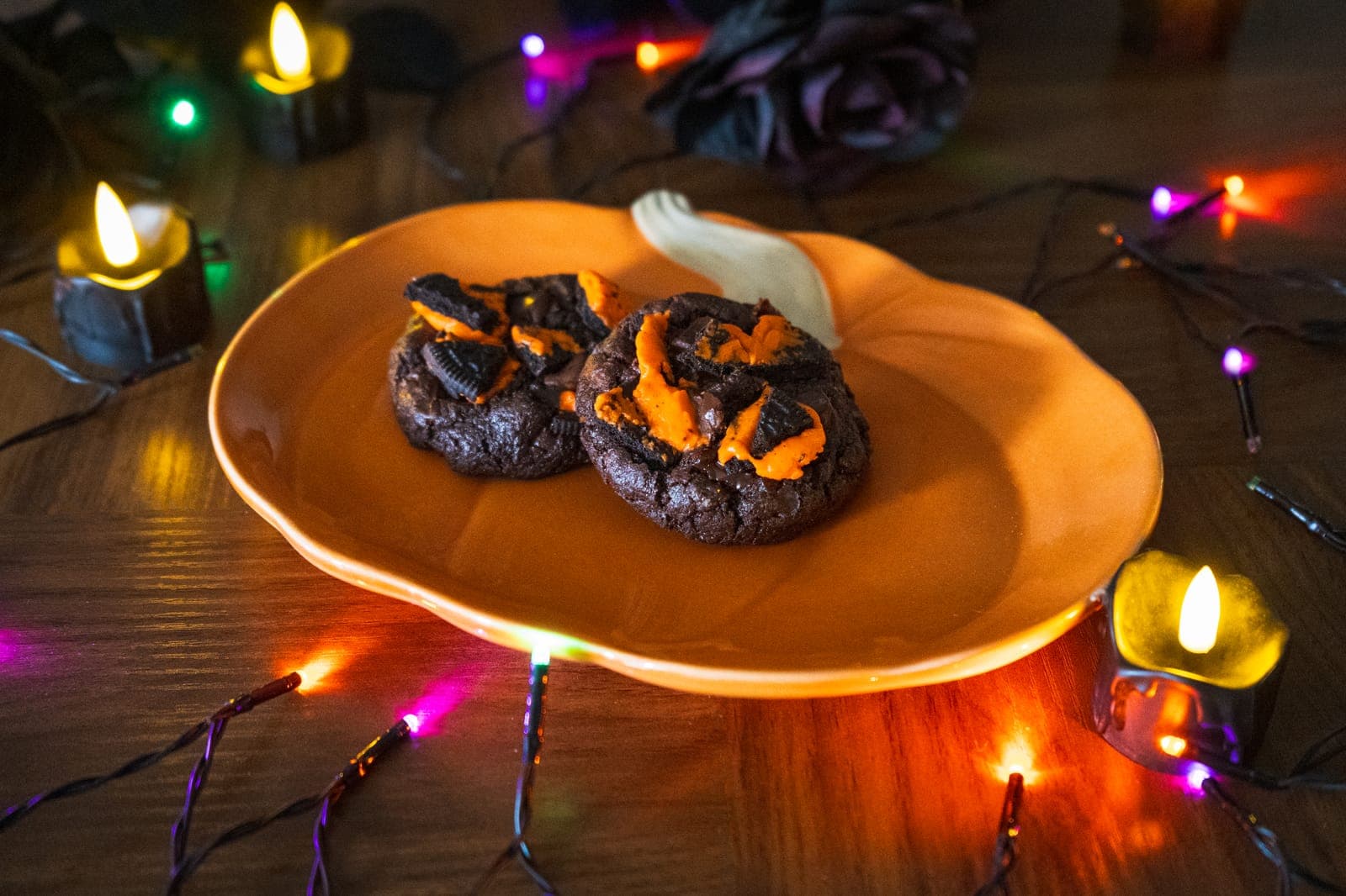 Two Oreo Brownie cookies with orange icing and Oreo pieces on a pumpkin plate