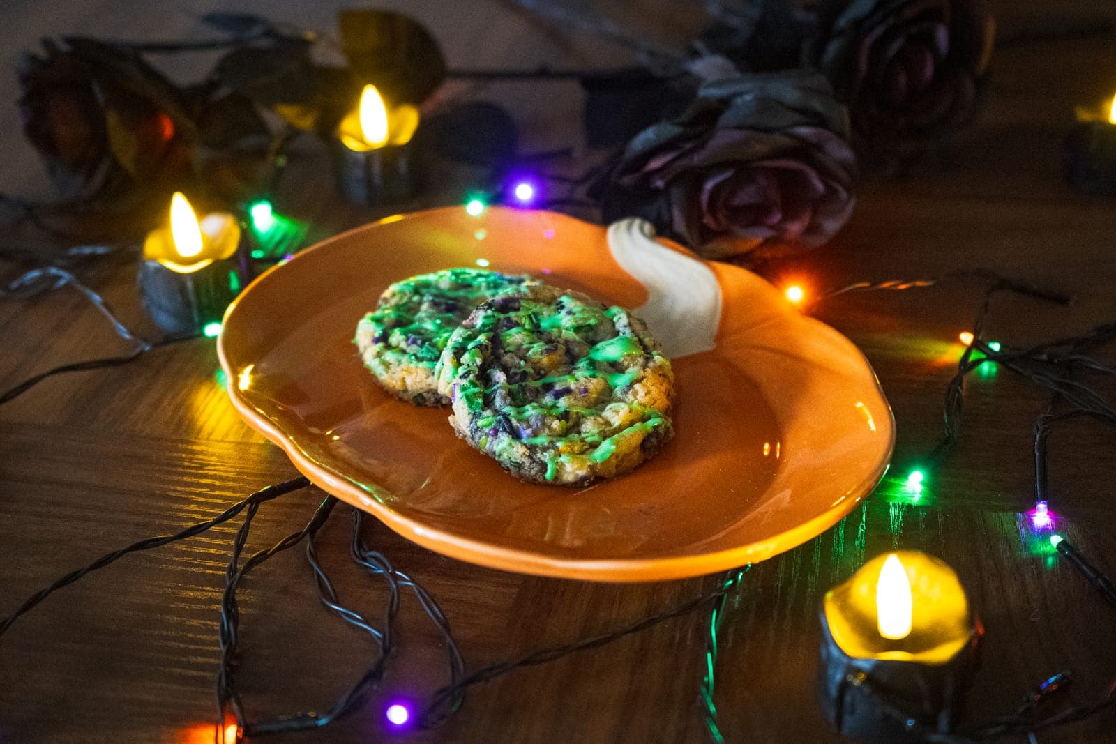 Two Slimy Sugar cookies with green drizzle and Halloween sprinkles on a pumpkin plate