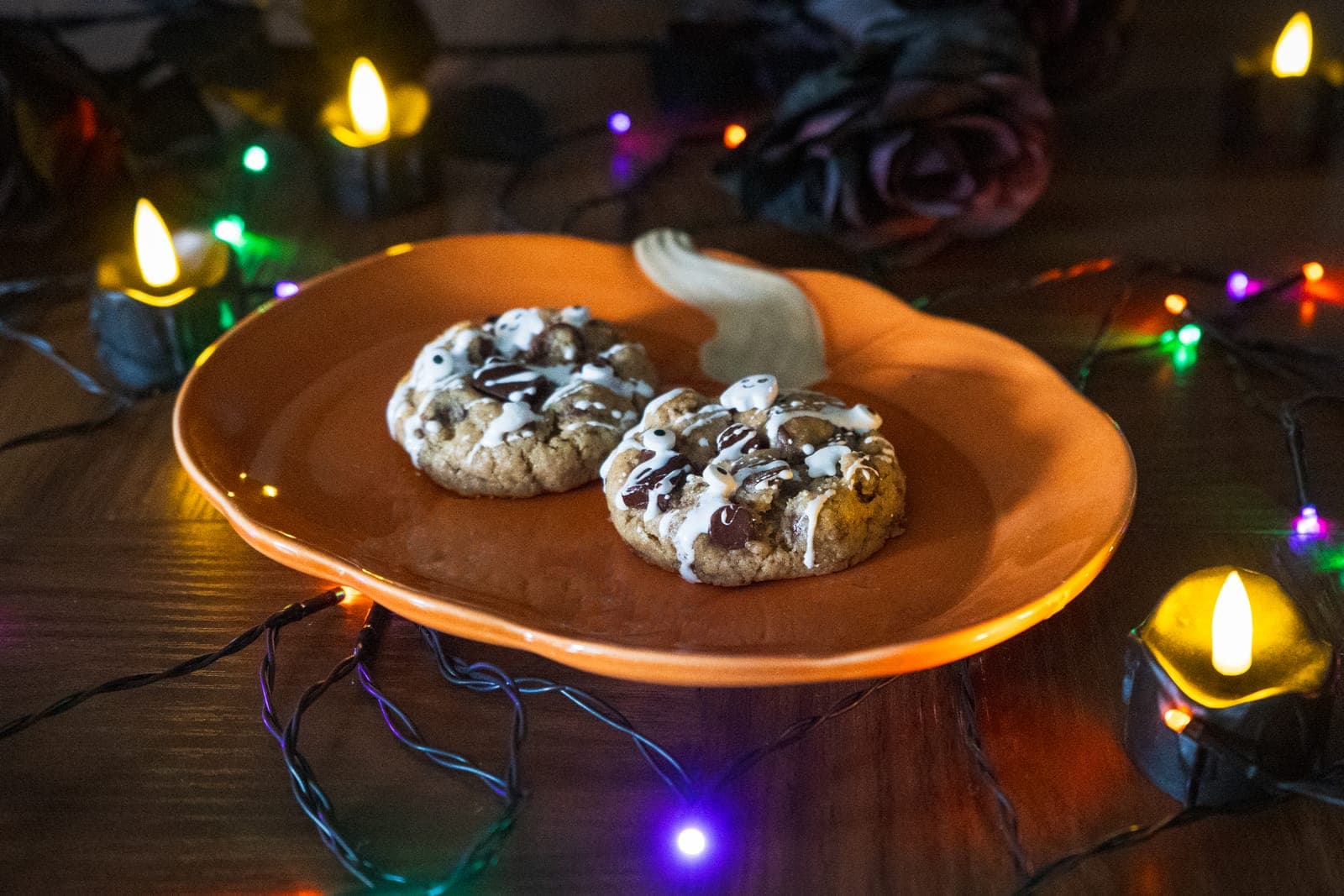 Two Spooky Chocolate Chip cookies with white drizzle and ghost sprinkles on a pumpkin plate