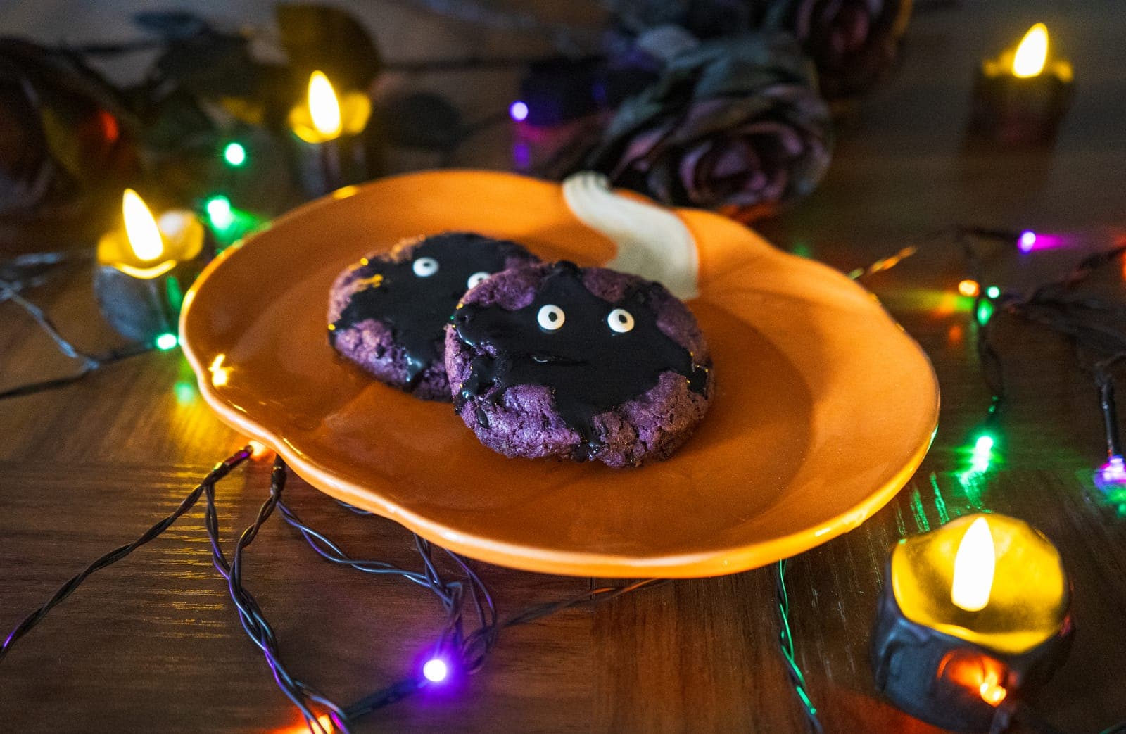 Two purple Ube Monster cookies with black icing and candy eyes on a pumpkin plate